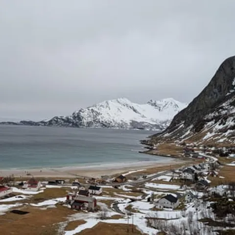 A fjord beach and small village below snow-covered peaks