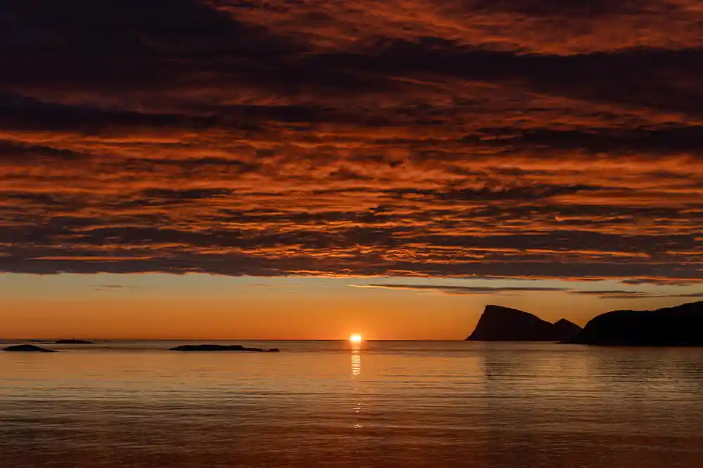 A deep orange midnight sun low over the sea