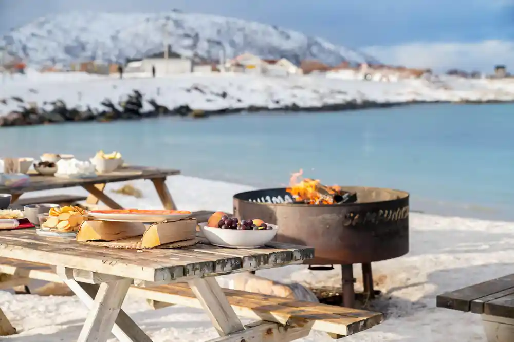 A fire pit burning beside a laid picnic table on the shore