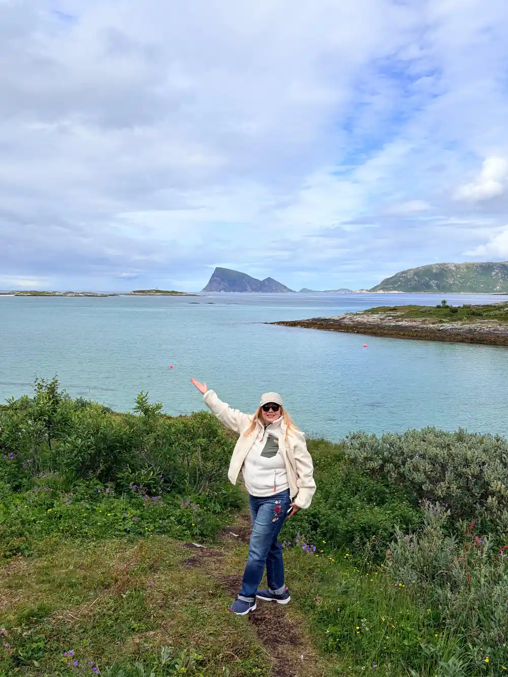 A guest with arms spread on a headland above turquoise water