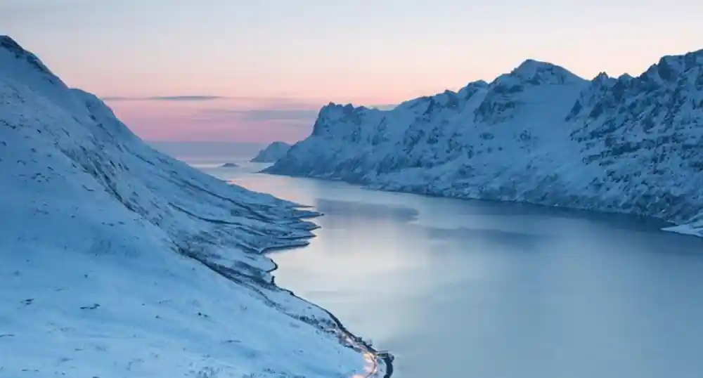 A long snow-covered ridge dropping to a pale fjord