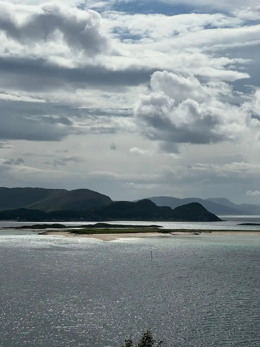 A pale beach and dark headland under grey cloud