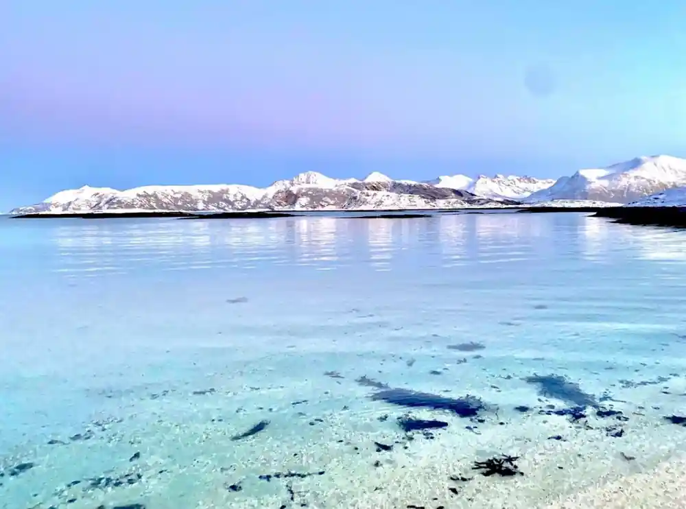 Pale turquoise shallows against snow-covered peaks