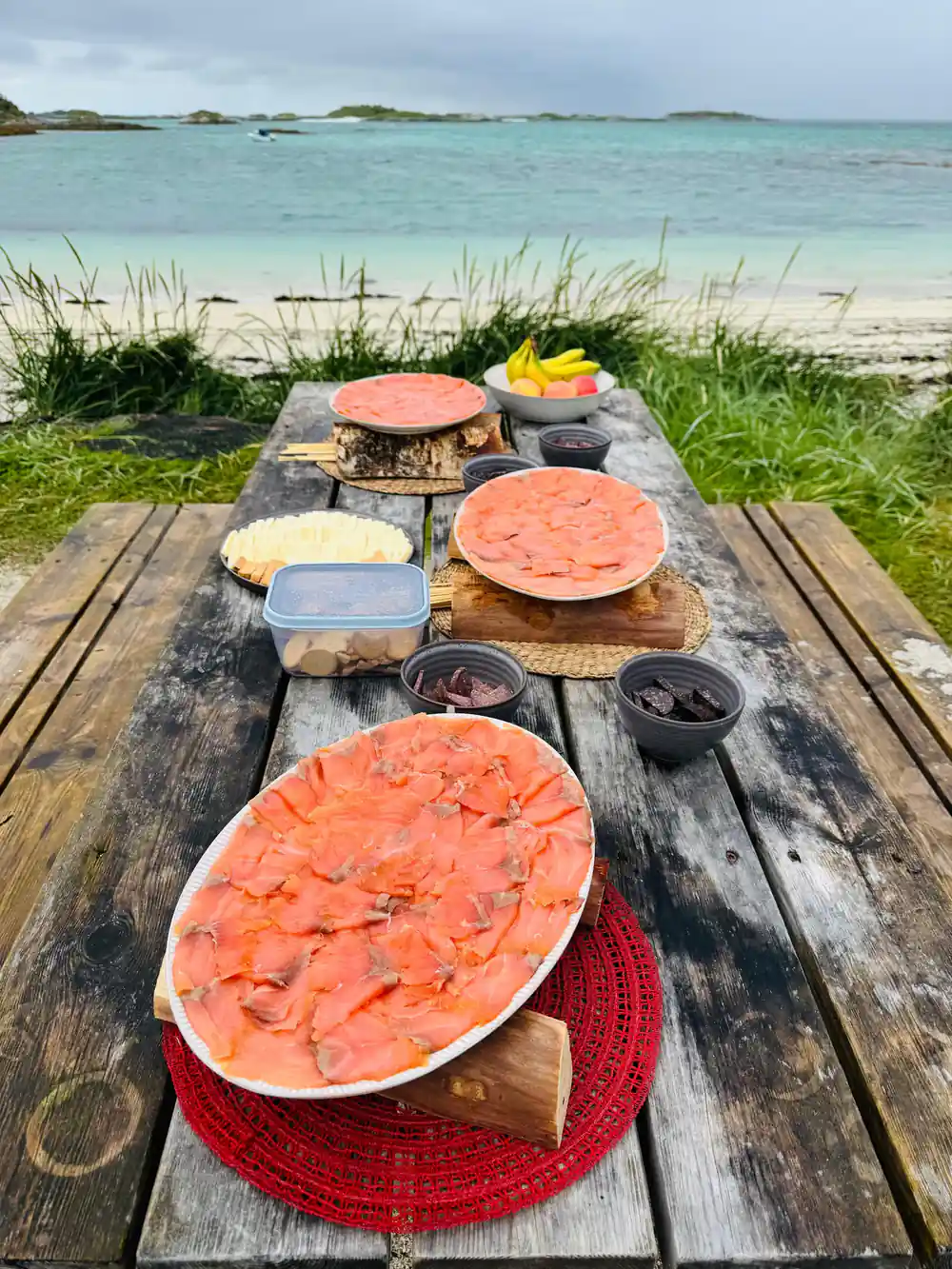 A picnic table set with salmon, bread and preserves by the sand