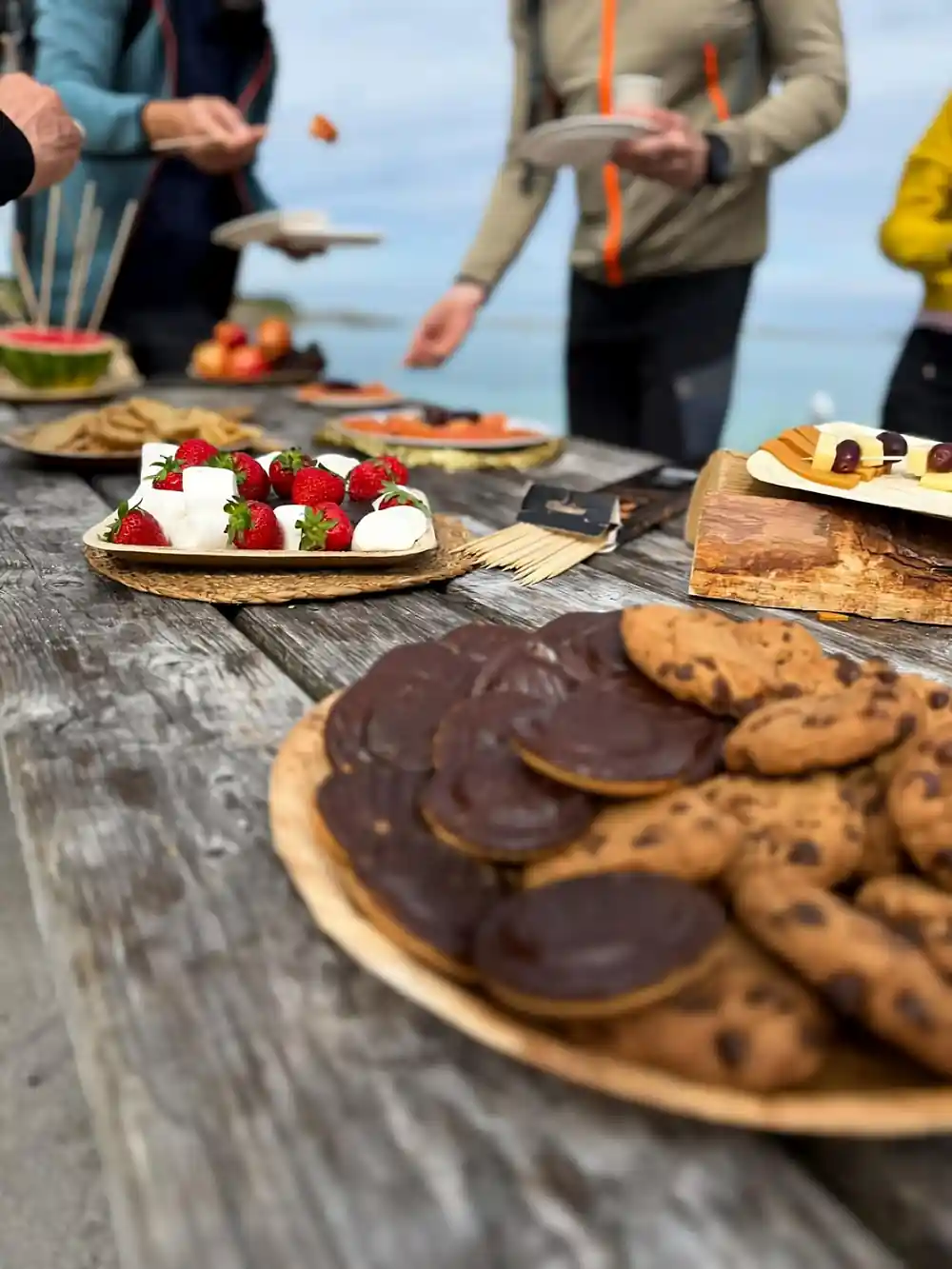 A picnic table spread with cookies, strawberries and fruit outdoors