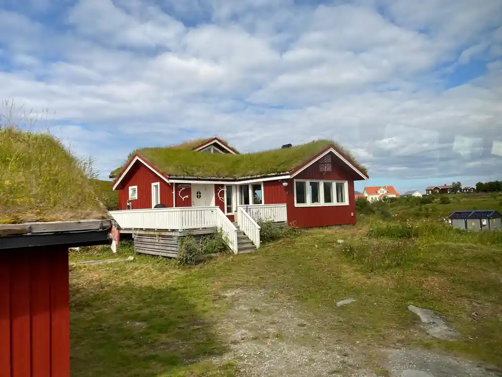 A red timber cabin with a turf roof on open grassland