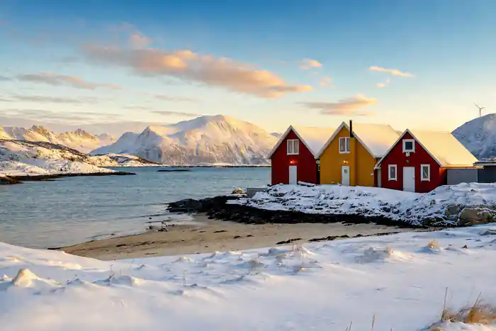 Red and yellow fishing cabins on a snowy shore below white mountains