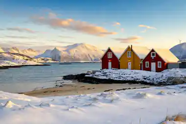 Red and yellow fishing cabins on a snowy shore below white mountains