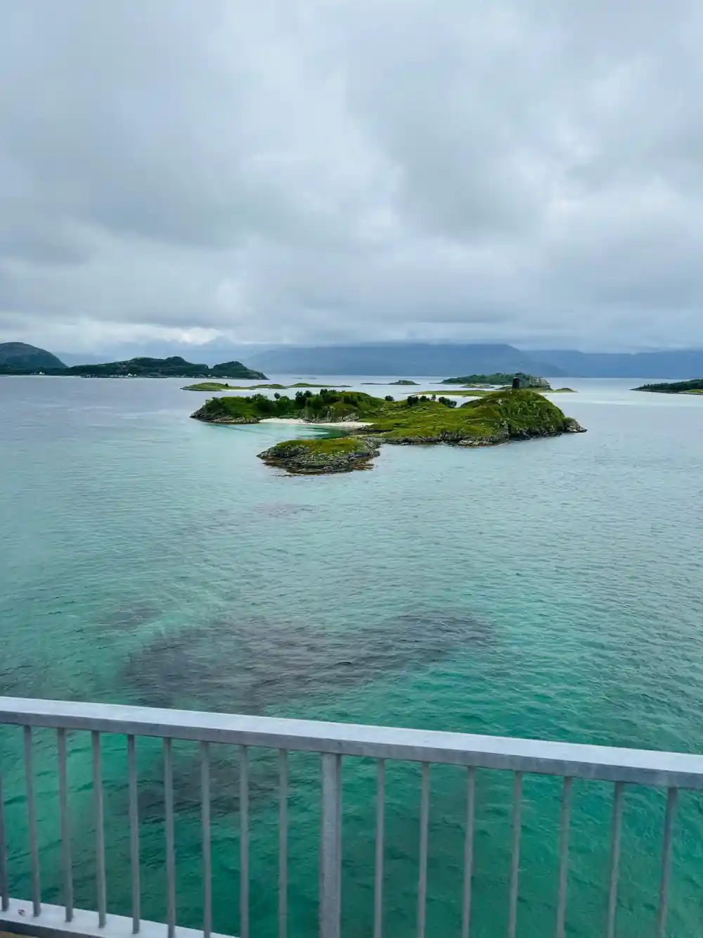 A viewing platform rail above clear green water and islets
